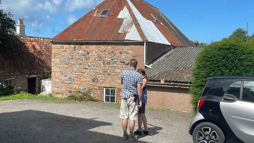 Two people inspect old stone building in sunlight.