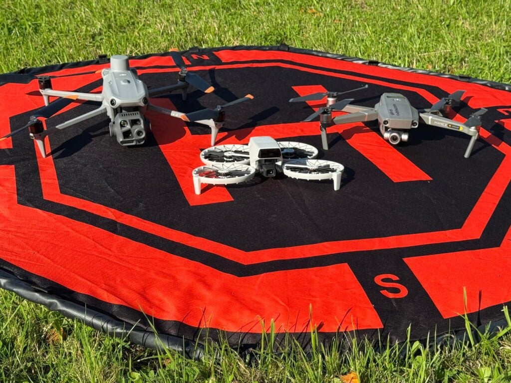 Three drones on a landing pad in grass.
