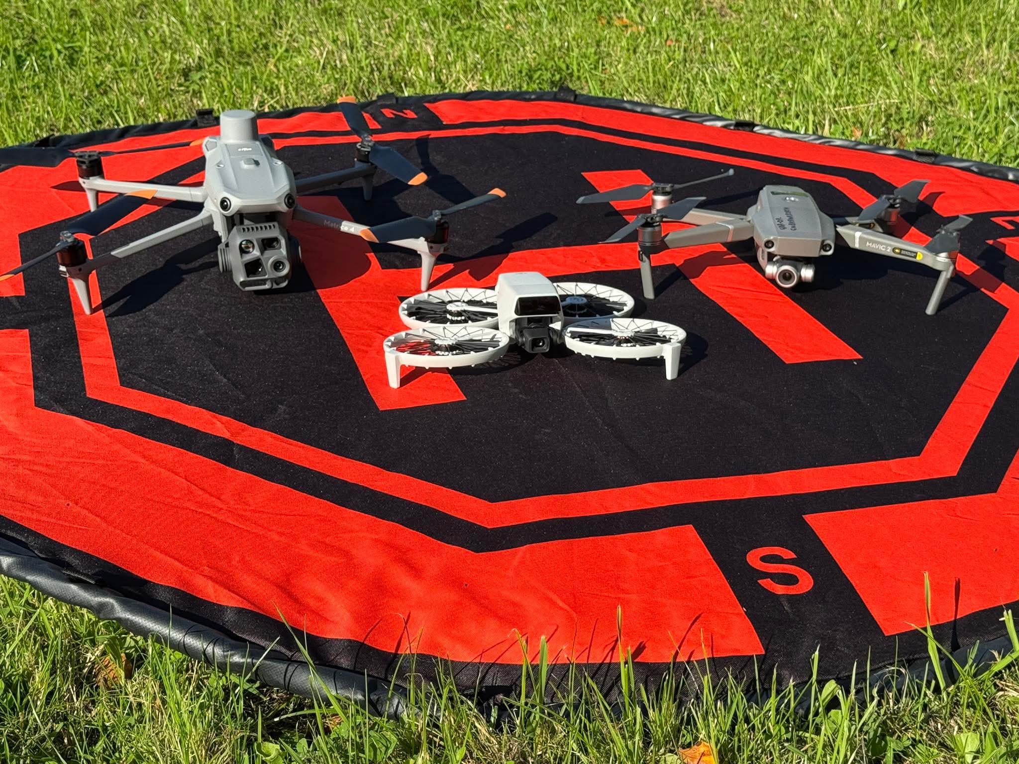 Three drones on a landing pad in grass.