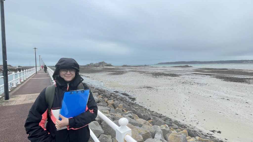 Person with clipboard on coastal walkway.