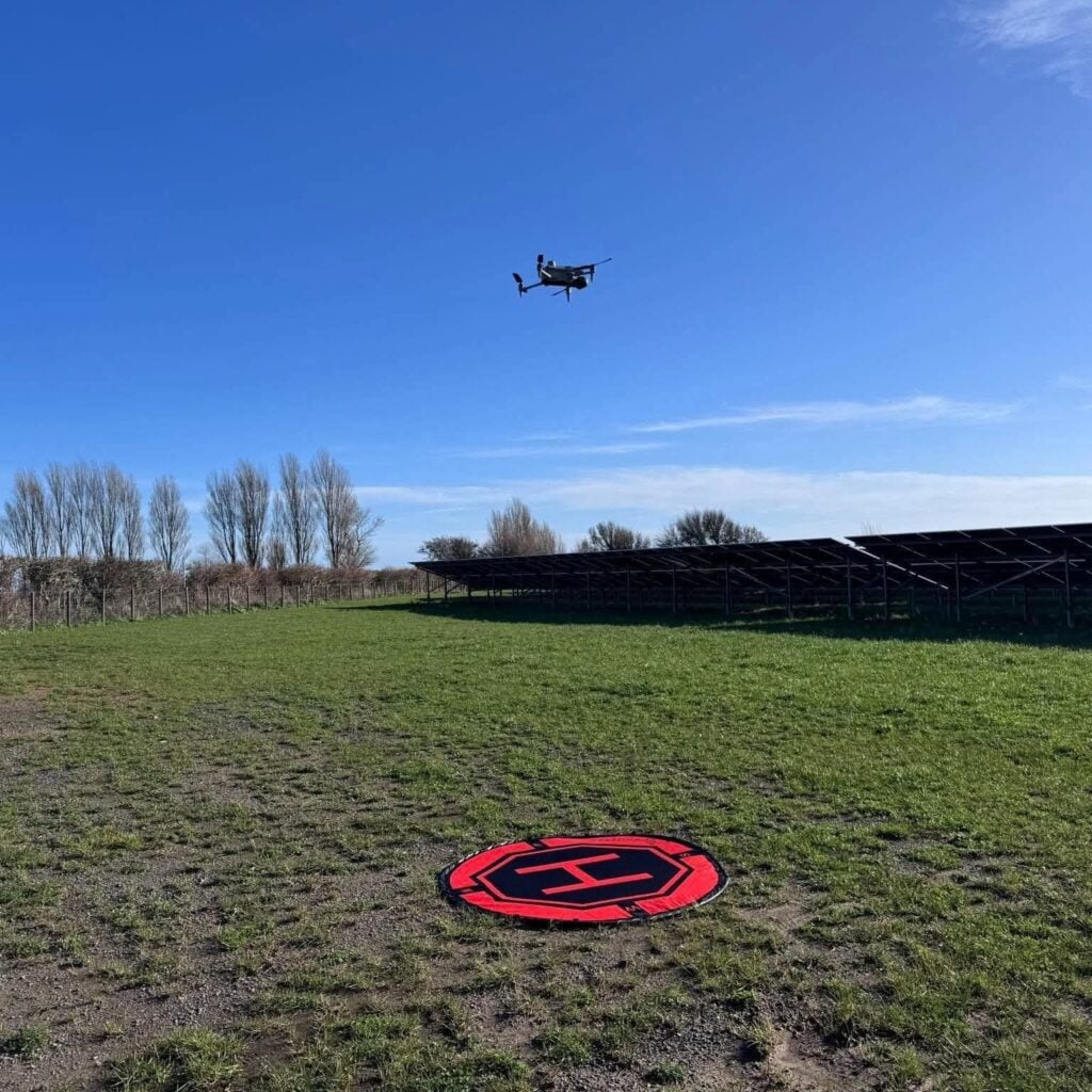 Drone flying over green field with landing pad.
